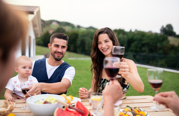 Portrait of family sitting at table outdoors on garden barbecue, eating and drinking wine.