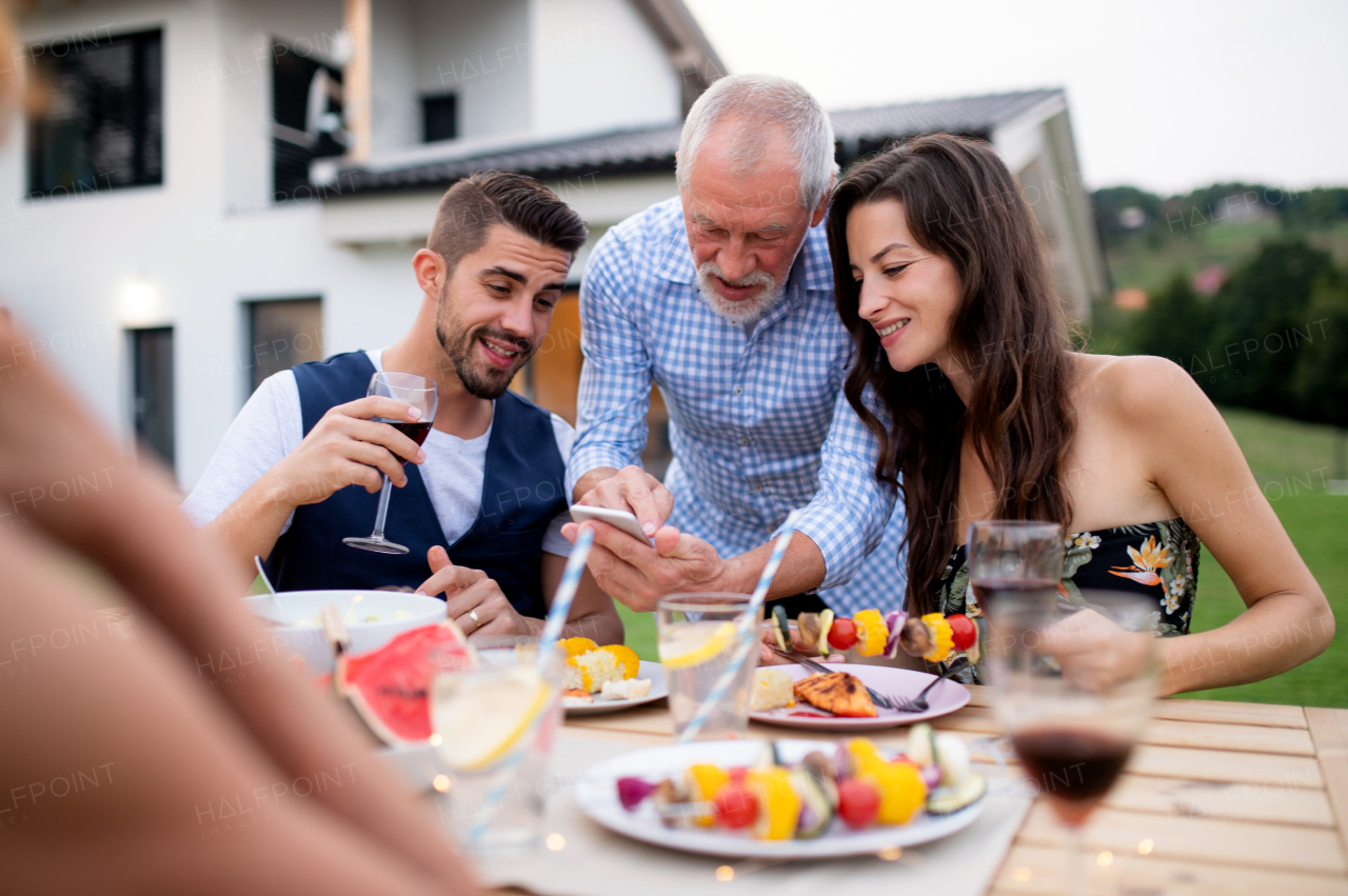 A portrait of people outdoors on family garden barbecue, using smartphone.