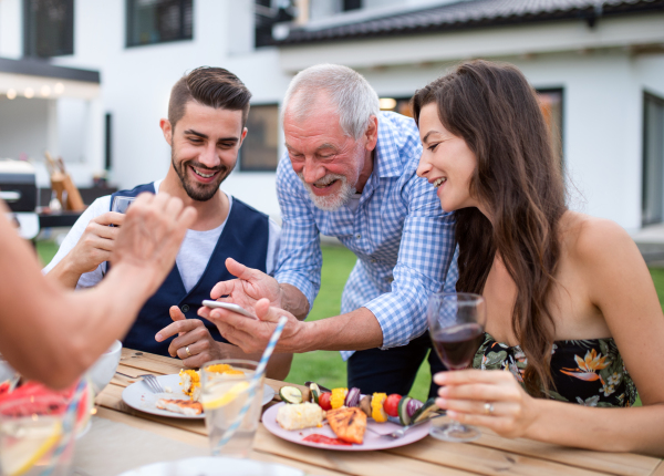 Portrait of people outdoors on family garden barbecue, taking selfie with smartphone.