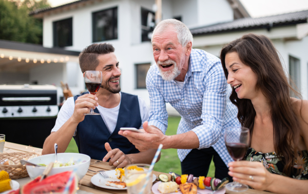 A portrait of people outdoors on family garden barbecue, using smartphone.