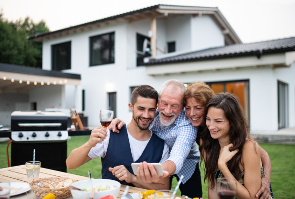 Portrait of people outdoors on family garden barbecue, taking selfie with smartphone.