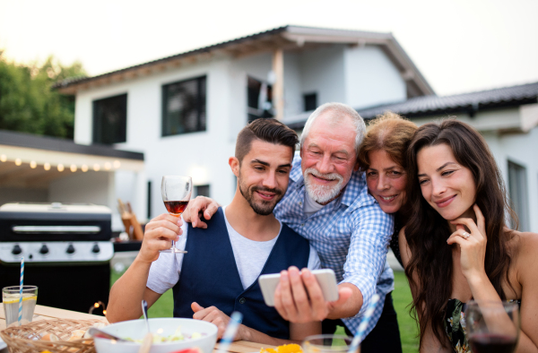 Portrait of people outdoors on family garden barbecue, taking selfie with smartphone.