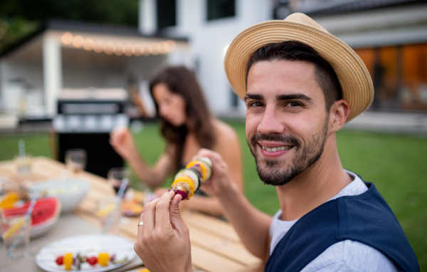 A young man sitting outdoors in back yard on garden barbecue, eating.