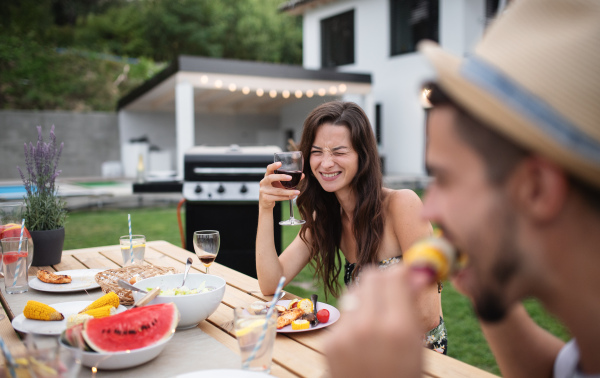 Portrait of family sitting at table outdoors on garden barbecue, eating and drinking wine.