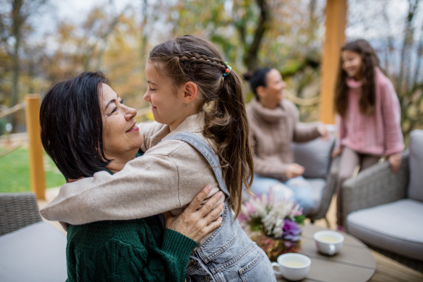 A happy little girl with grandmother sitting wrapped in blanket outdoors in patio in autumn