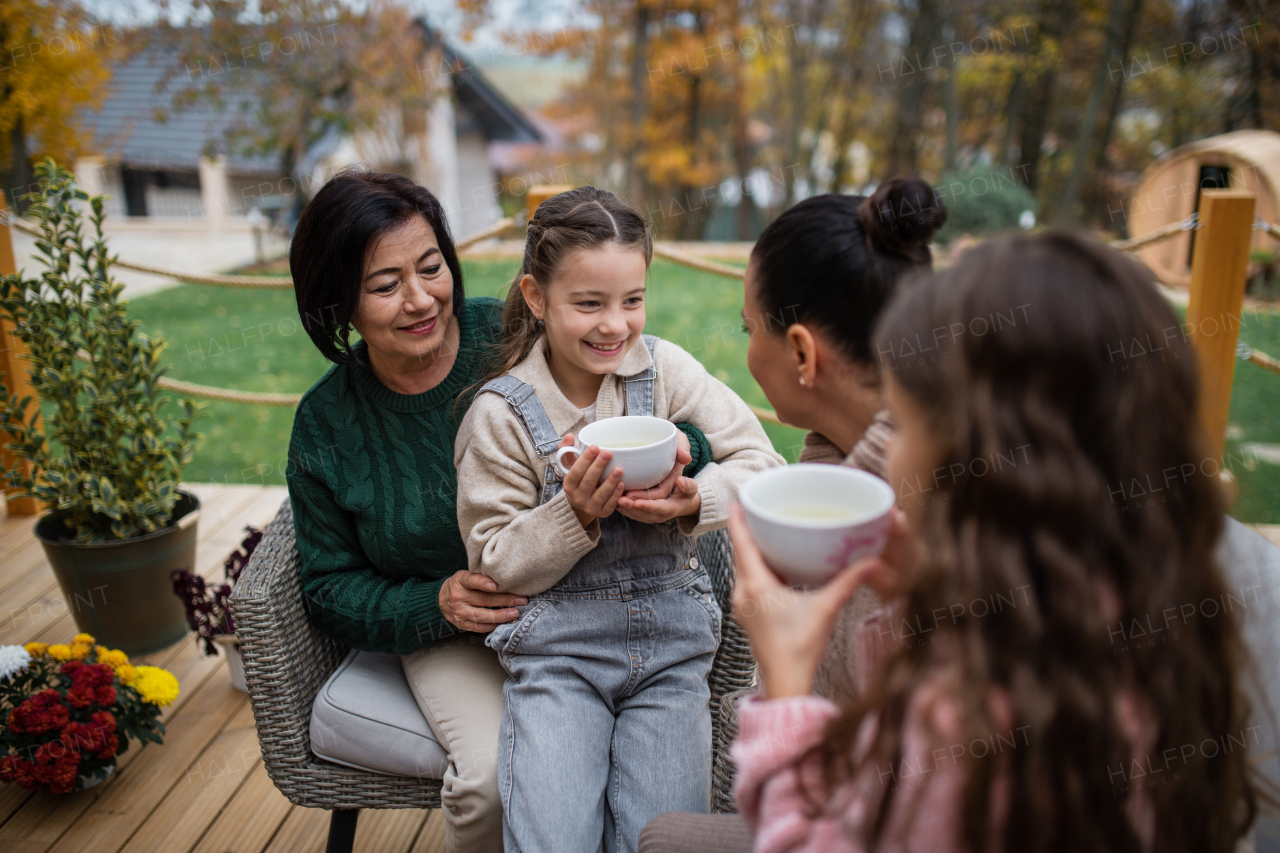 Two happy sisters with a mother and grandmother sitting and drinking tea outdoors in patio in autumn.