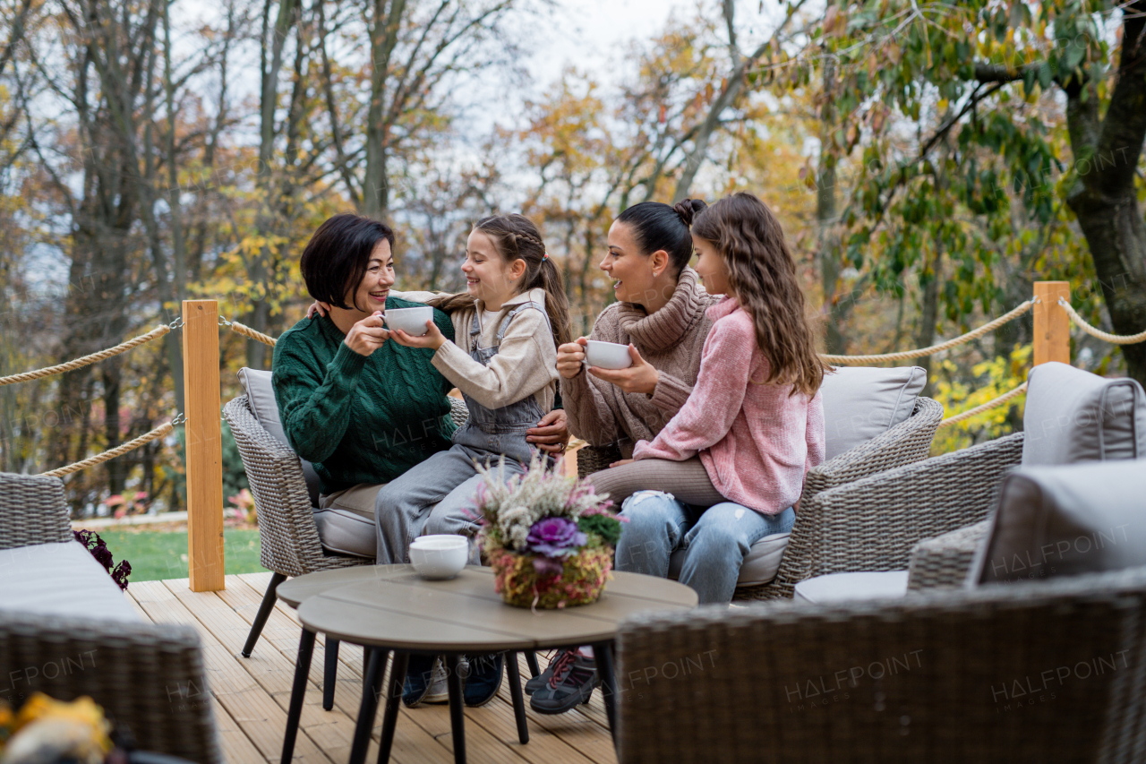 Two happy sisters with a mother and grandmother sitting and drinking tea outdoors in patio in autumn.