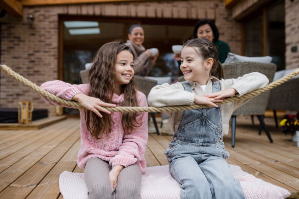 Two happy sisters with a mother and grandmother sitting outdoors in patio in autumn.