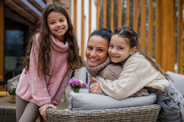 Two happy sisters with a mother embracing and looking at camera outdoors in patio in autumn.