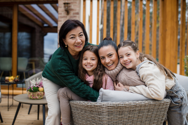 Two happy sisters with a mother and grandmother embracing and looking at camera outdoors in patio in autumn.