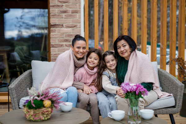 Three generations females sitting and drinking tea and looking at a camera outdoors in patio in autumn