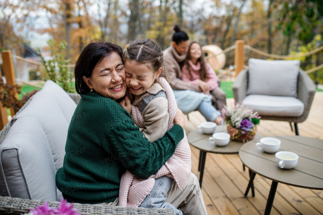 A happy little girl with grandmother sitting wrapped in blanket outdoors in patio in autumn