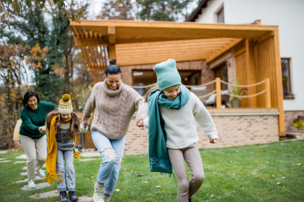 Two happy sisters with a mother and grandmother holding hands and running outdoors in garden in autumn