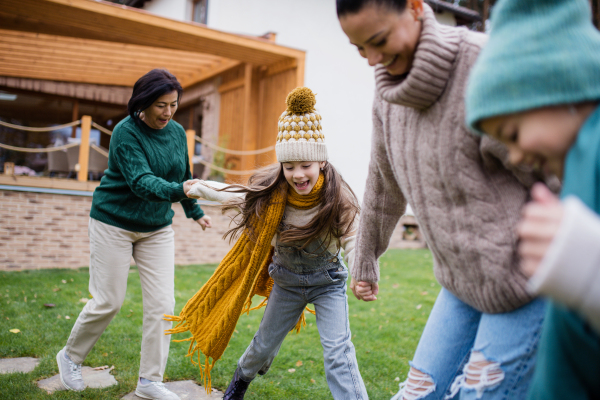 Two happy sisters with a mother and grandmother holding hands and running outdoors in garden in autumn