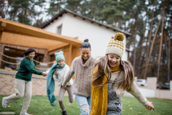 Two happy sisters with a mother and grandmother holding hands and running outdoors in garden in autumn