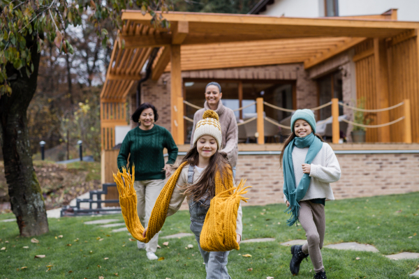 Two happy sisters with a mother and grandmother holding hands and running outdoors in garden in autumn