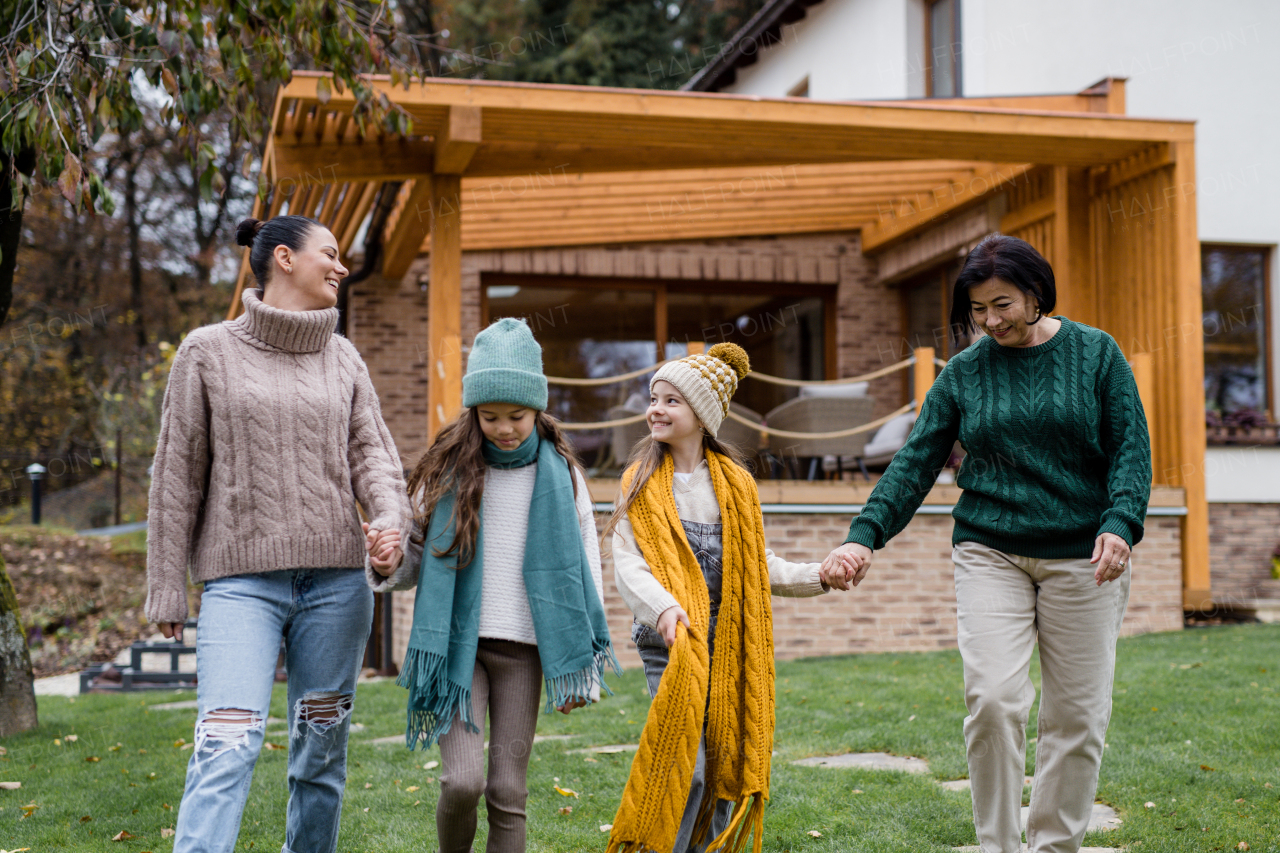 Two happy sisters with a mother and grandmother walking and holding hands outdoors in garden in autumn