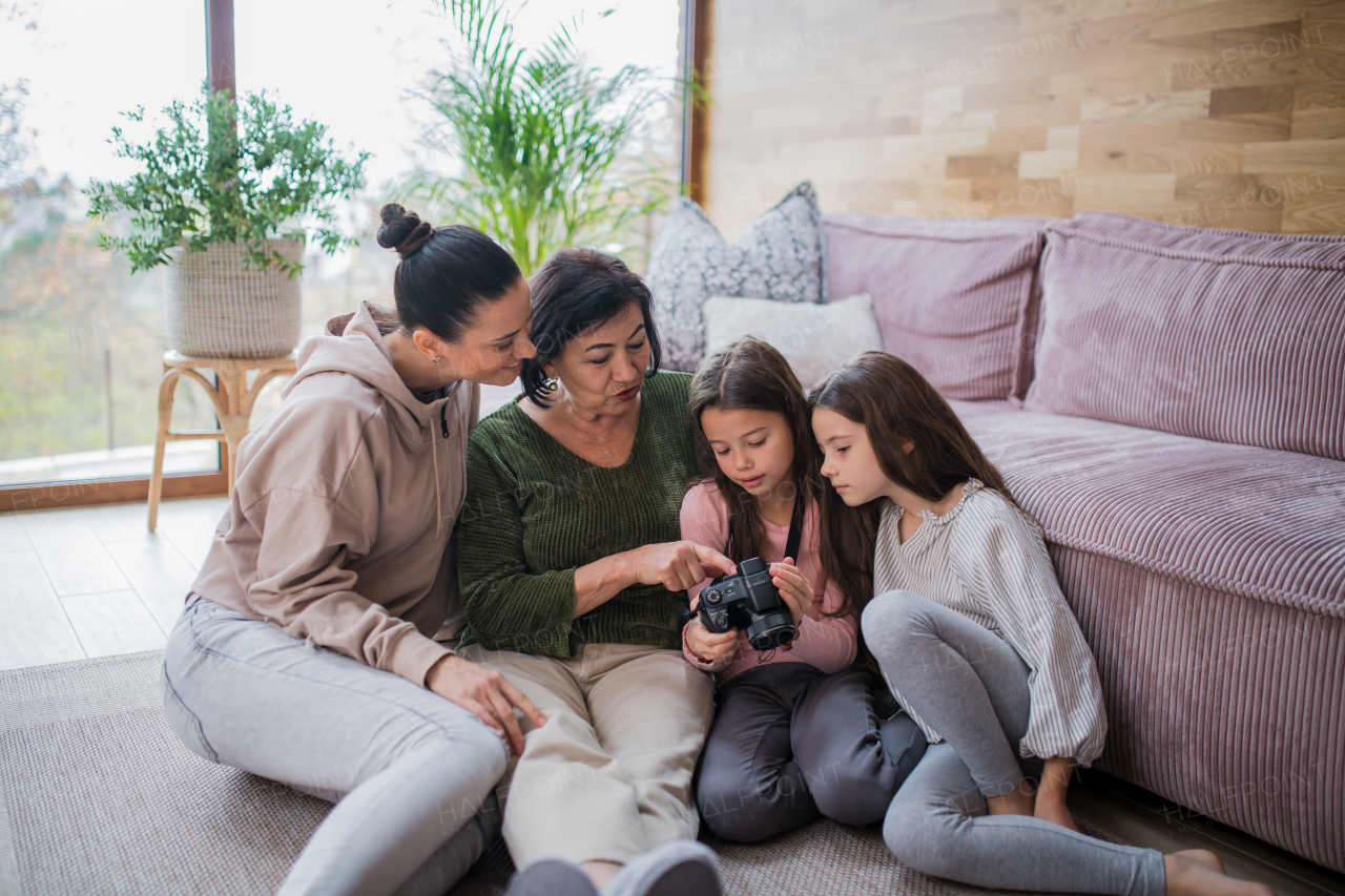 Two happy sisters with a mother and grandmother sitting on floor and learning to use camera at home