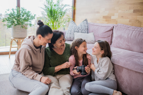 Two happy sisters with a mother and grandmother sitting on floor and learning to use camera at home