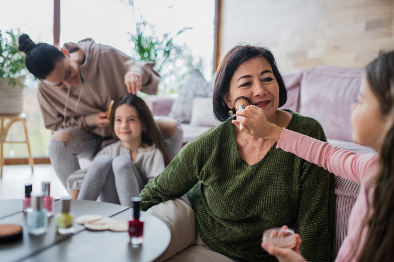 Two happy sisters with a mother and grandmother combing hair and doing make up together at home