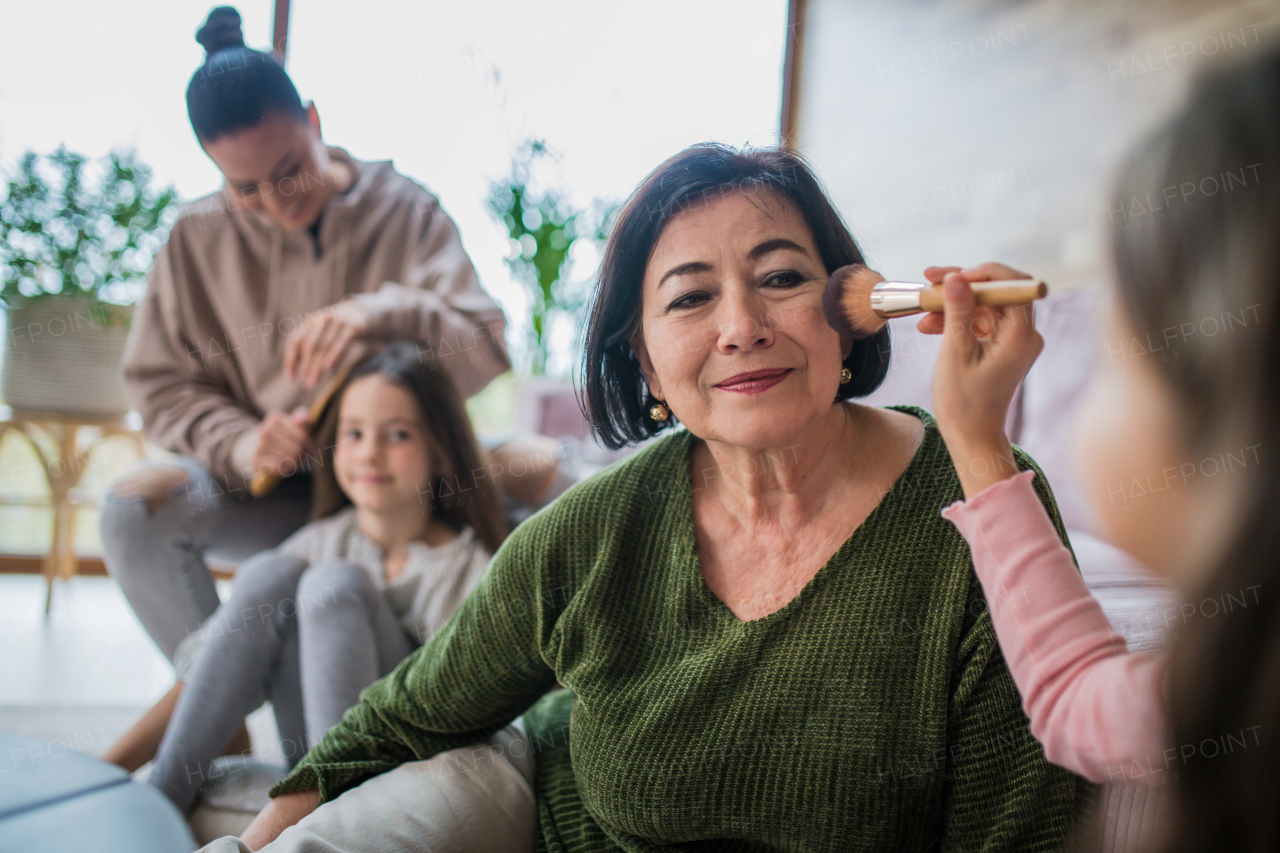 Two happy sisters with a mother and grandmother combing hair and doing make up together at home