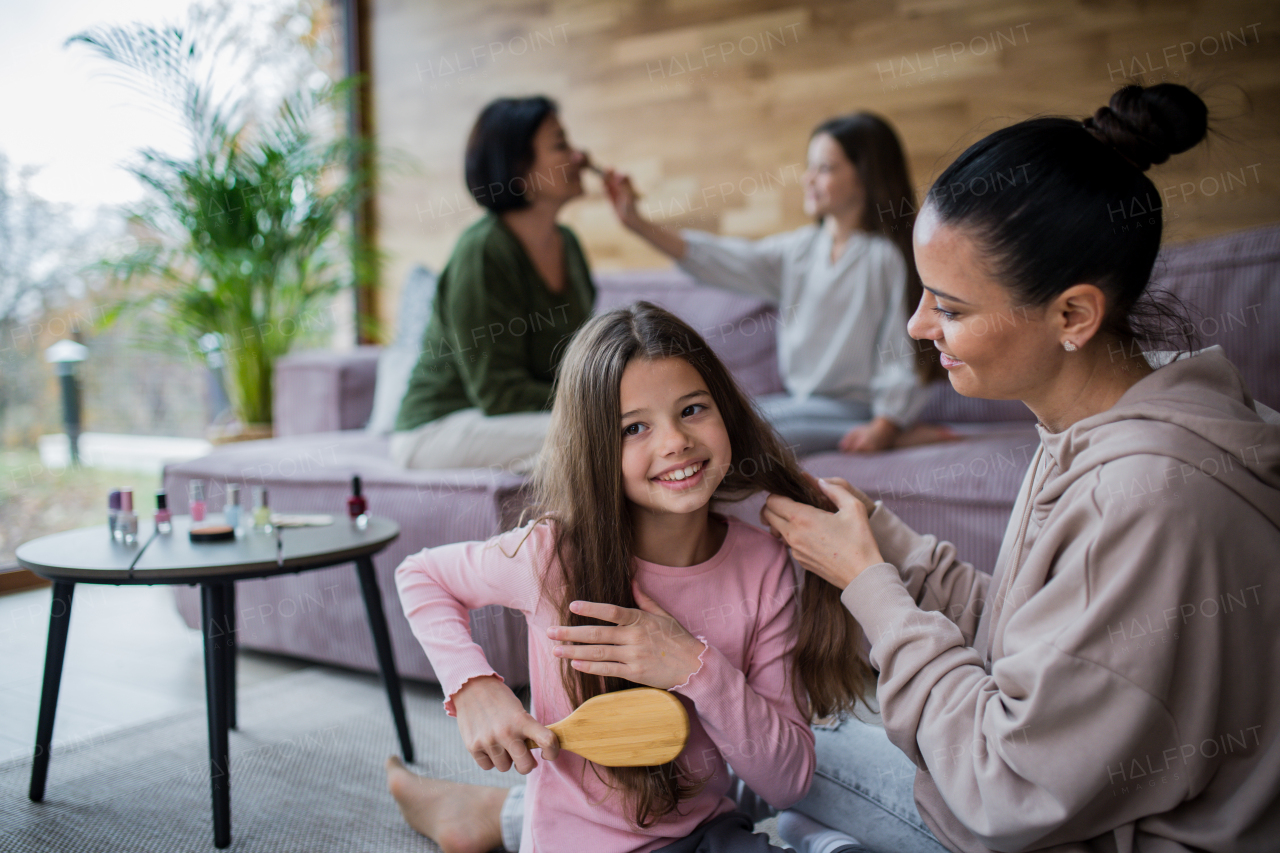 Two happy sisters with a mother and grandmother combing hair and doing make up together at home