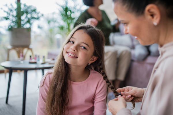 A mother making a plait to little daughter at home.