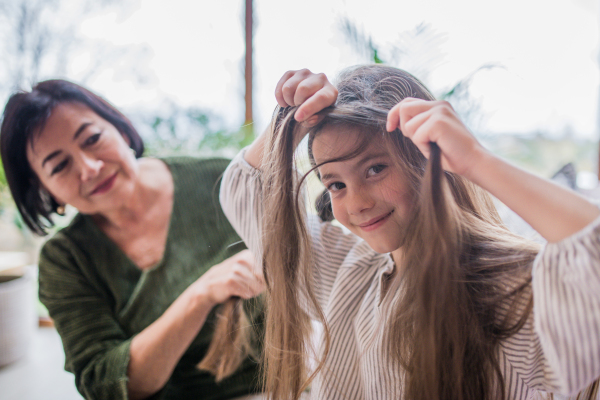 A grandmother helping her little granddaughter with making a hairstyle.