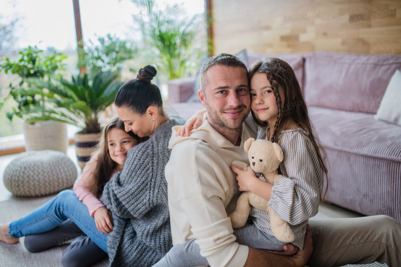 Two happy sisters with a mother and father sitting on floor hugging and looking at camera at home