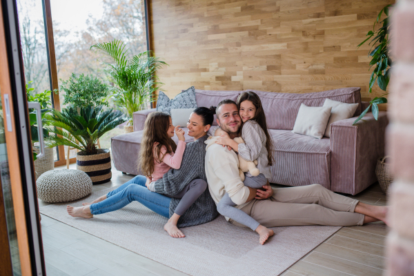 Two happy sisters with a mother and father sitting on floor hugging and looking at camera at home