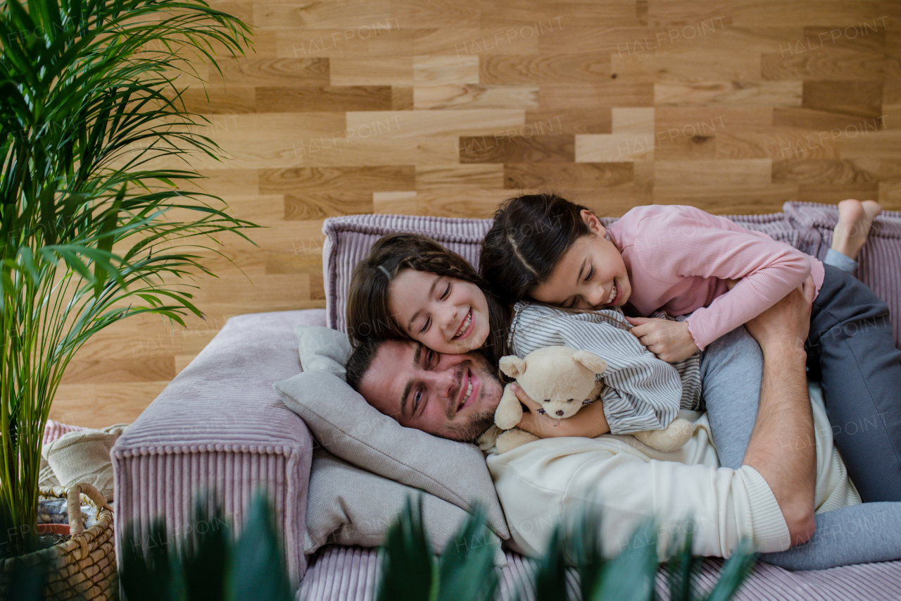 Two happy sisters having fun with a father, lying on sofa at home.