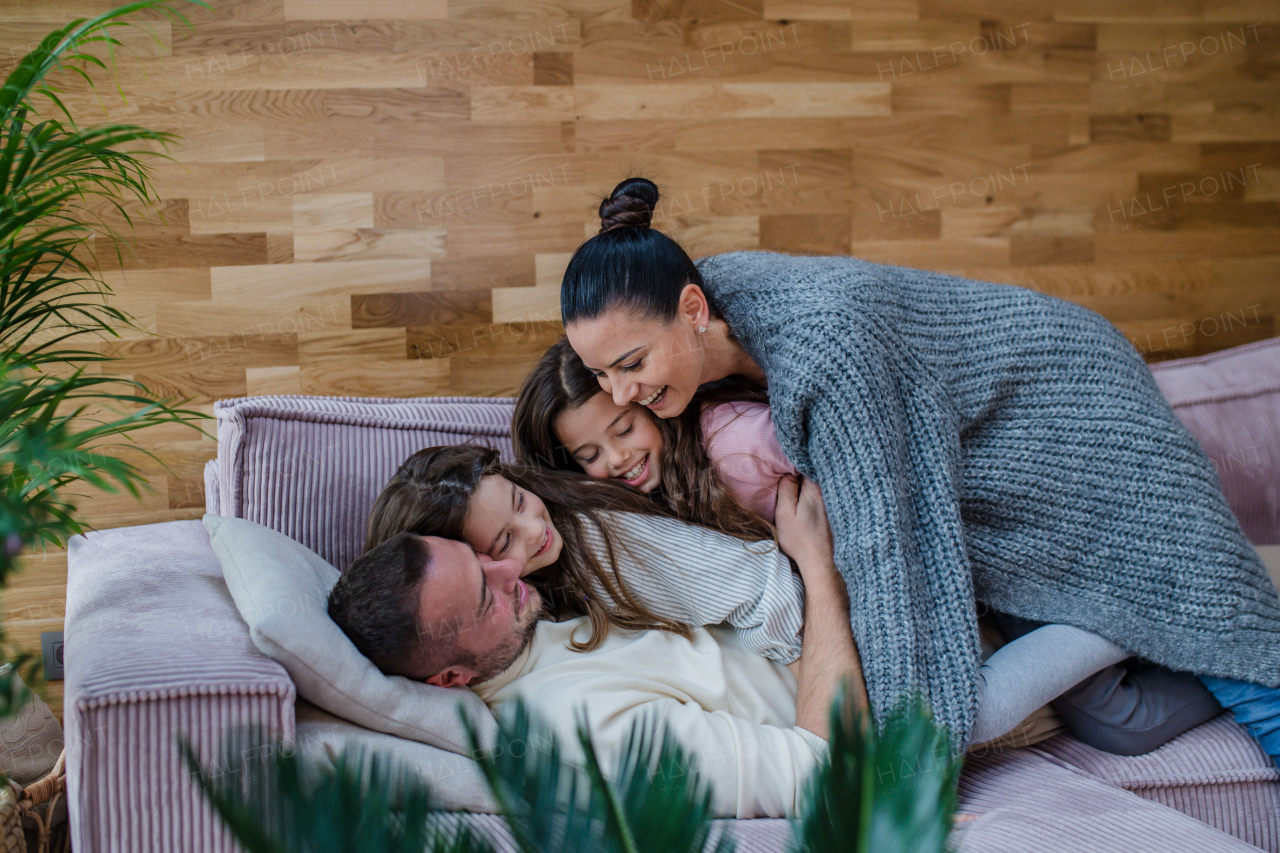 Two happy sisters having fun with a father nad mother, lying on sofa at home.