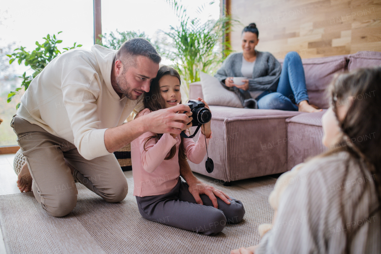 Two happy sisters with father sitting on floor and learning to use camera at home