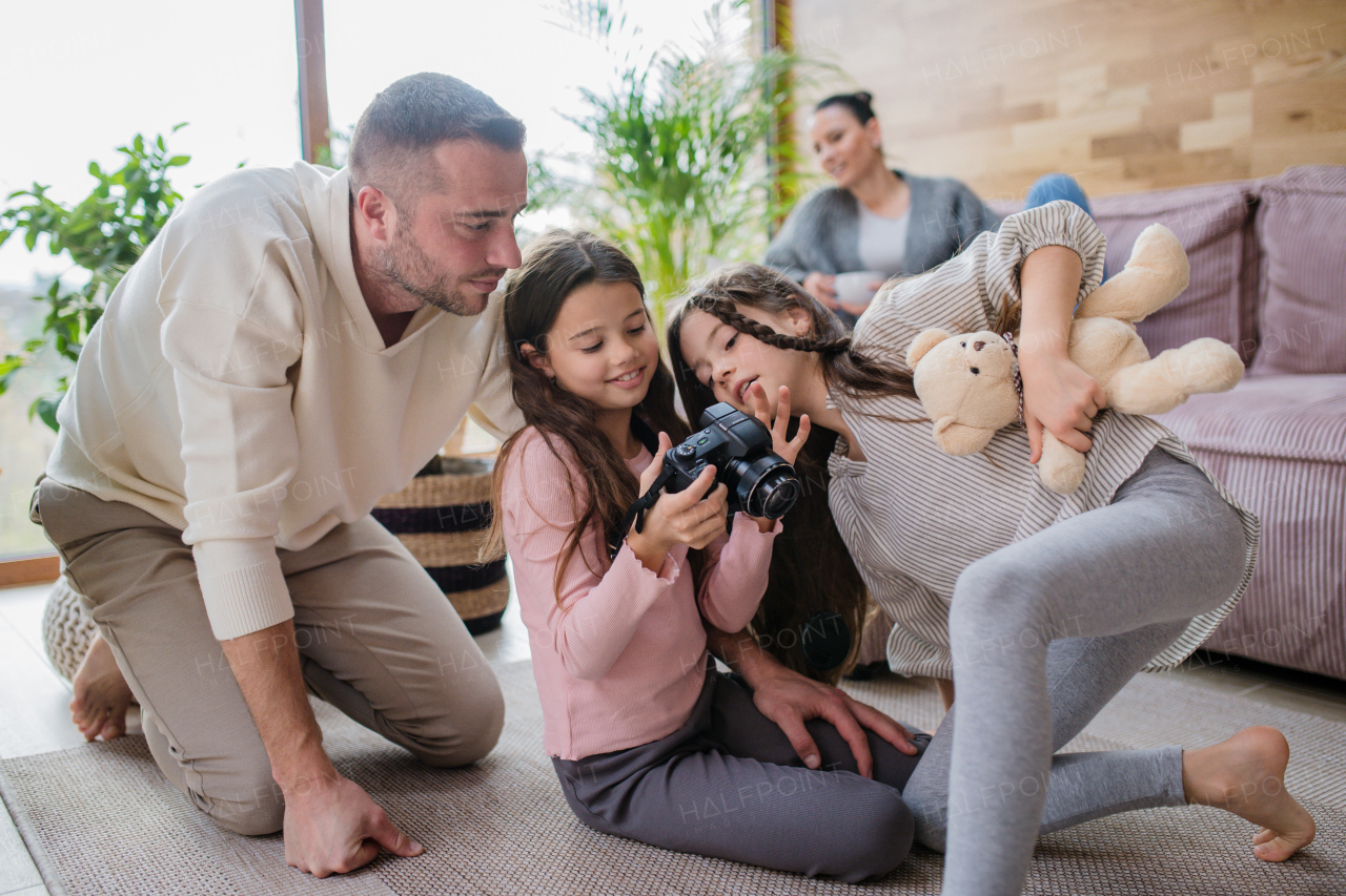 Two happy sisters with father sitting on a floor and learning to use camera at home