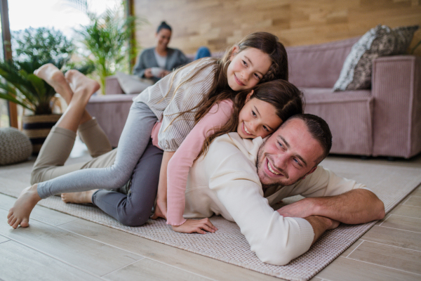 Two happy sisters having fun with a father, lying on his back with mother at background at home