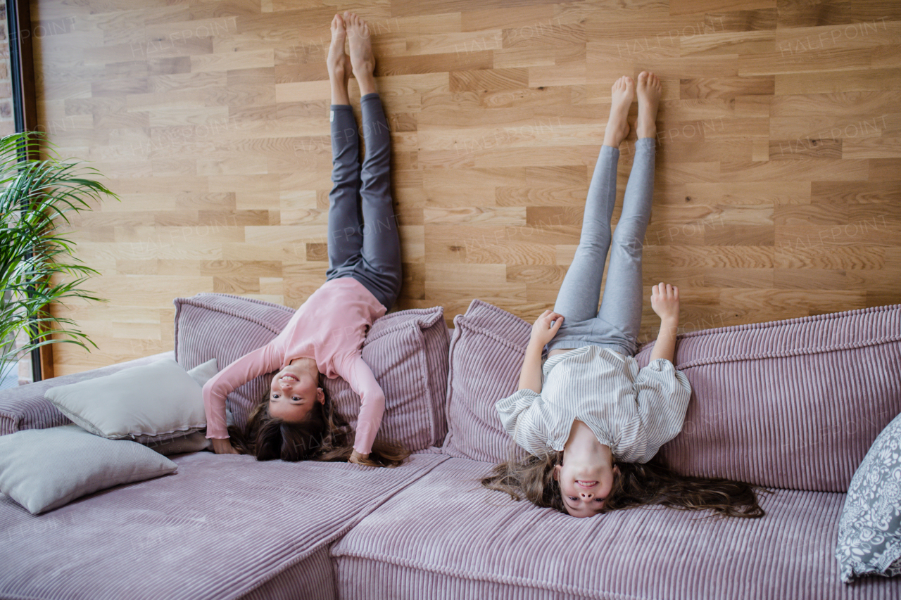 Happy little sisters doing head stand on a sofa at home.