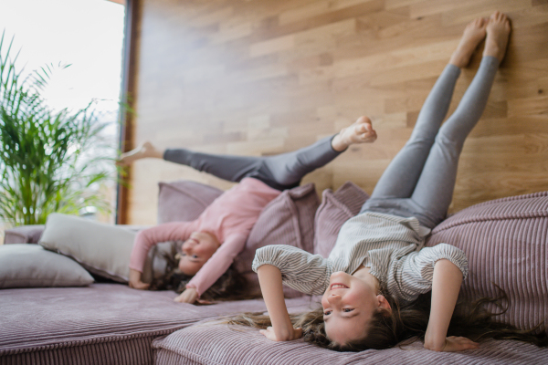 Happy little sisters doing head stand on a sofa at home.