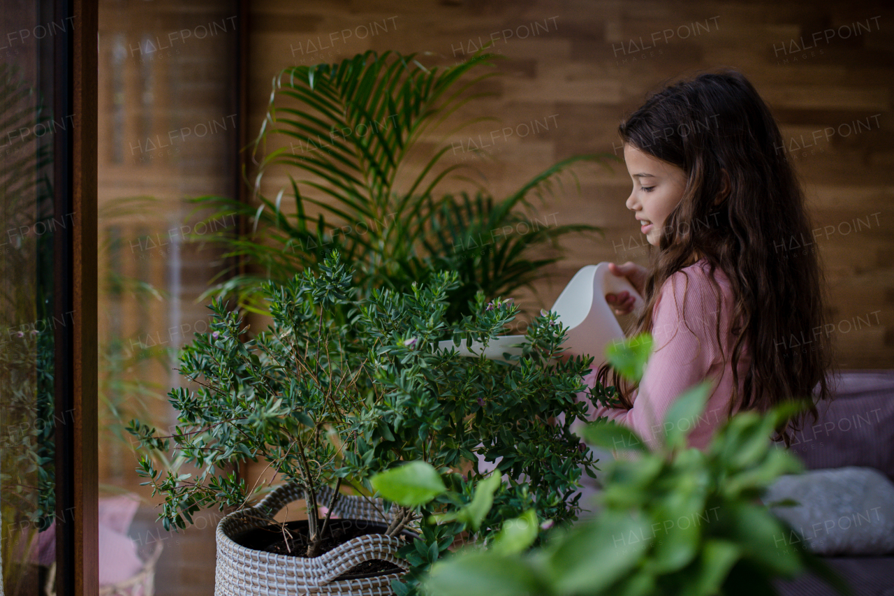 A happy little girl watering flowers with watering can indoors at home.