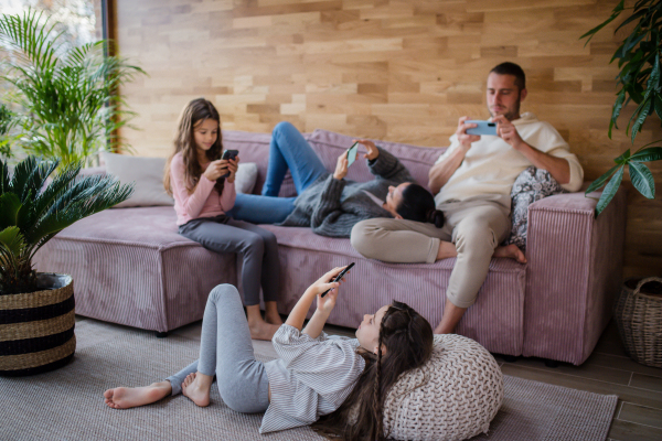 A family with two little daughters, everyone is using mobile phone in the living room.