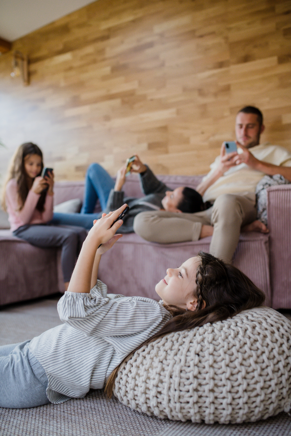 A family with two little daughters, everyone is using mobile phone in the living room.