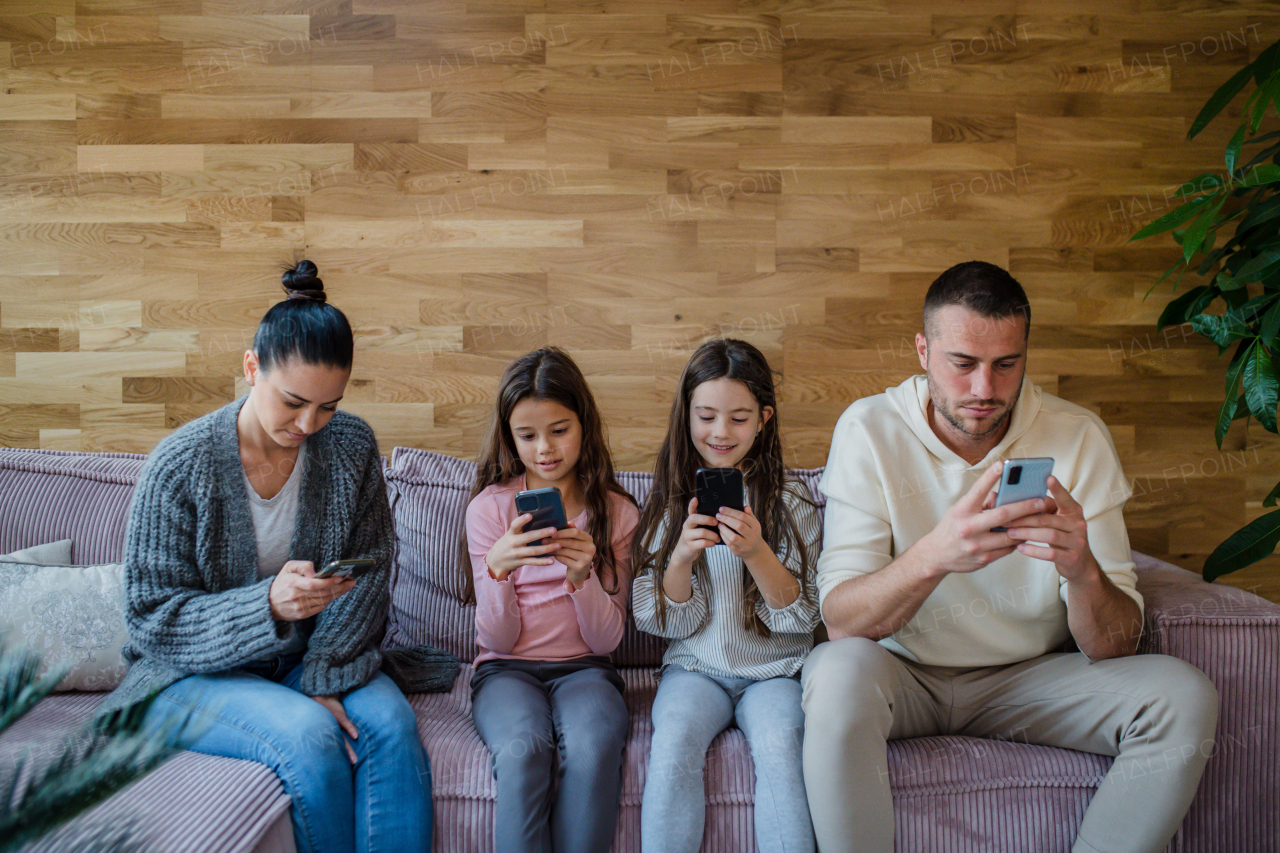 A family with two little daughters, everyone is using mobile phone in the living room.