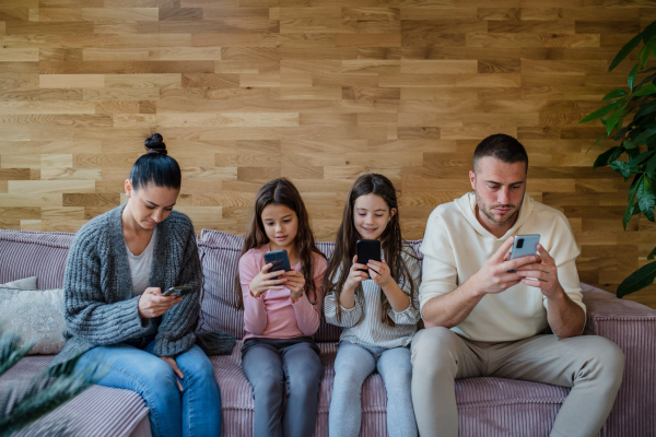 A family with two little daughters, everyone is using mobile phone in the living room.