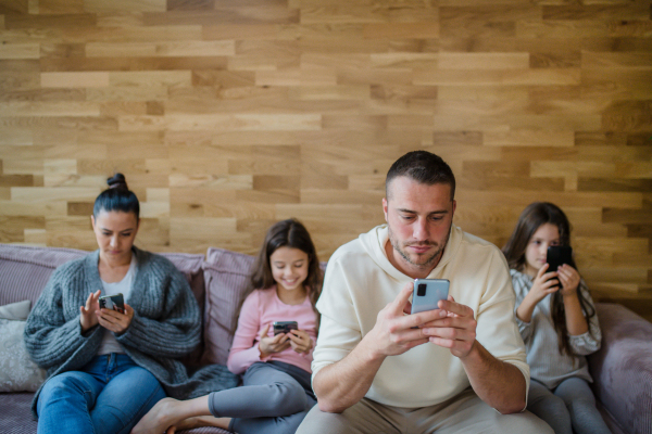 A family with two little daughters, everyone is using mobile phone in the living room.