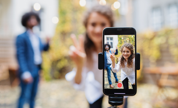 Portrait of young couple making video with smartphone outdoors on street, social media concept.