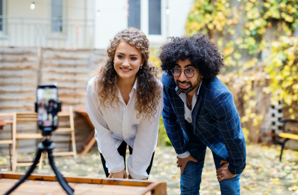 Portrait of young couple with smartphone making video for social media outdoors in park.