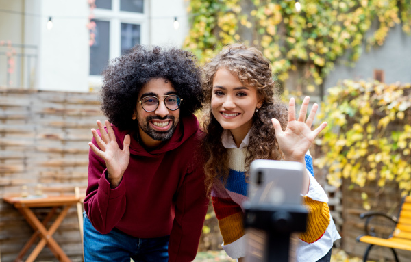 Portrait of young couple with smartphone making video for social media outdoors on street.