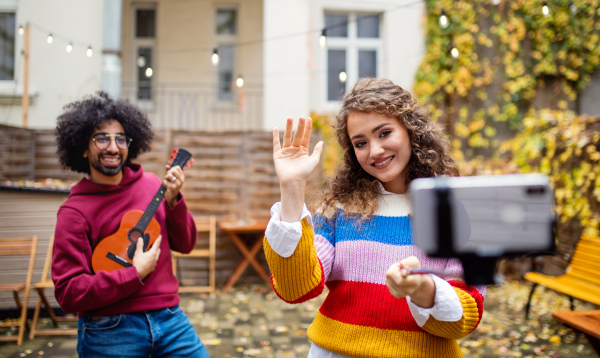 Portrait of young couple with smartphone making video for social media outdoors on street.