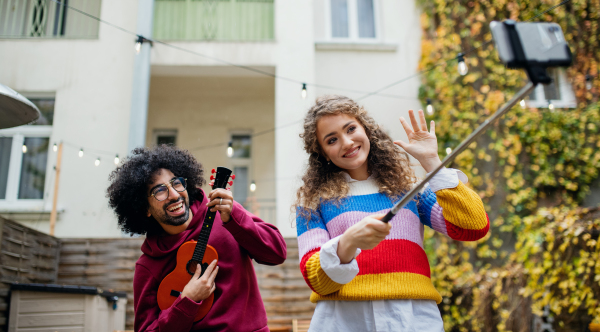 Portrait of young couple with smartphone making video for social media outdoors on street.