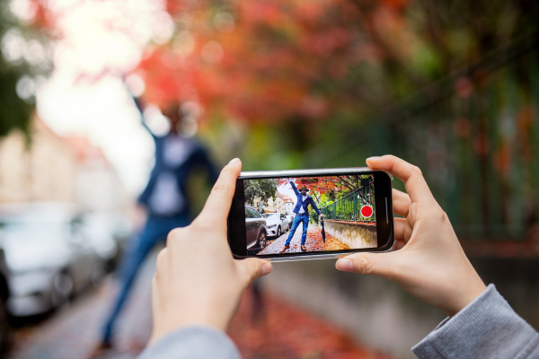 A young couple with smartphone making video for social media outdoors on street.