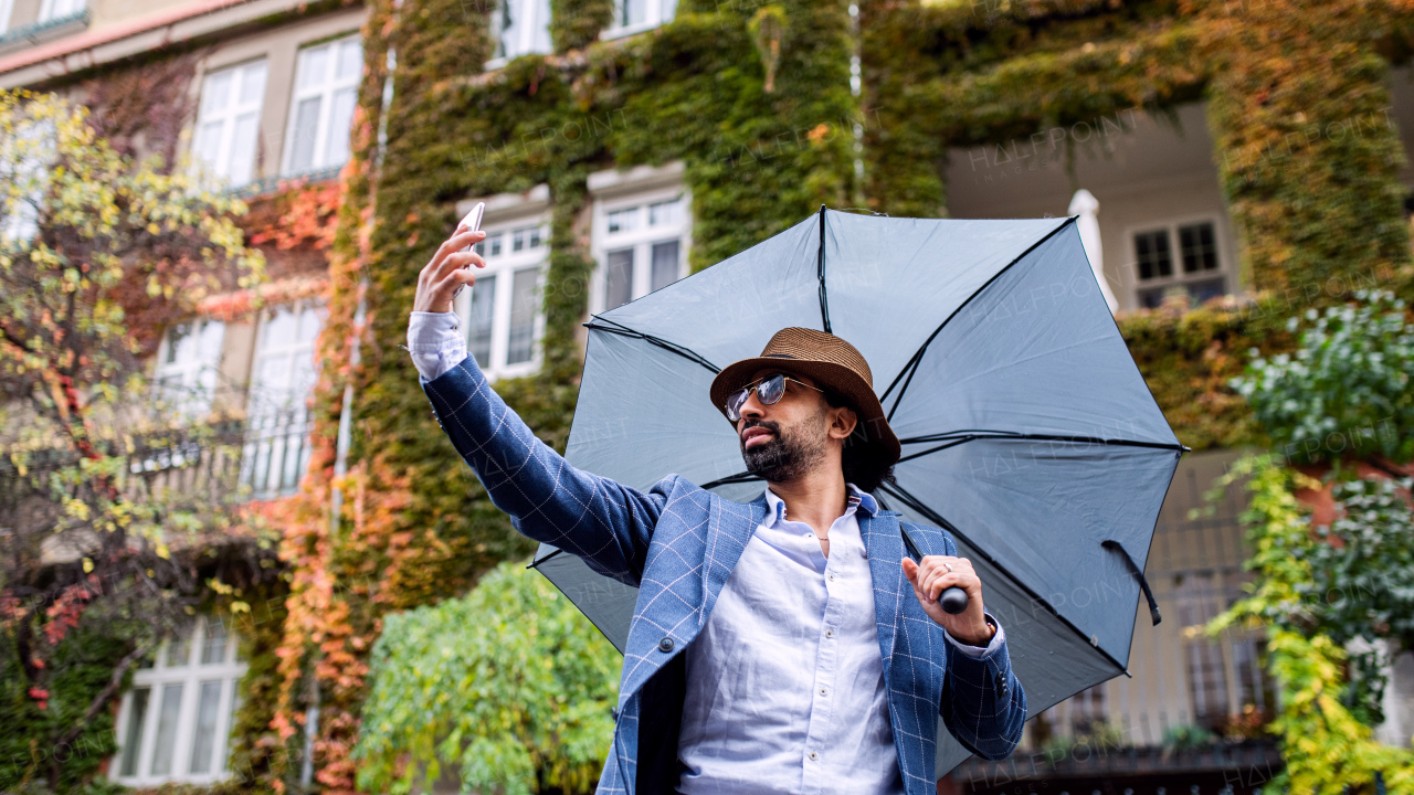 Portrait of young man with umbrella making video outdoors on street, social media concept.